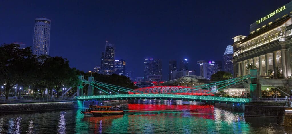 Jorden Rundt – Cavenagh Bridge og The Fullerton Hotel oplyst ved Singapore River med bumboat